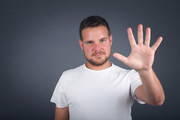 Young man standing against gray wall showing and pointing up with fingers number five while smiling confident and happy.