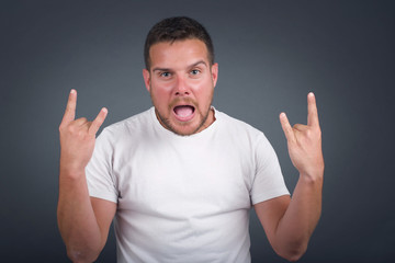 Naklejka premium Born to rock this world. Joyful man in fashionable clothes screaming out loud and showing with raised arms horns or rock gesture, expressing excitement of being on concert of band.