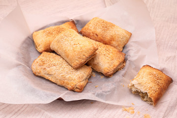 Homemade freshly baked puff pastry pies stuffed with mushrooms and eggs sprinkled with sesame seeds on white parchment. Delicious appetizer.