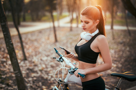 beautiful girl in shorts and bras reads message on phone near bicycle at sunset in park