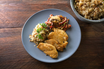 chicken filet with cauliflower rice and vegetable ragout from bell pepper and mushroom, healthy diet meal on a blue plate on a dark rustic wooden table from above, copy space