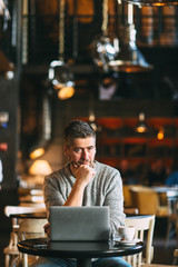Middle-aged man working on a laptop computer, sitting at the cafeteria, lifestyle concept