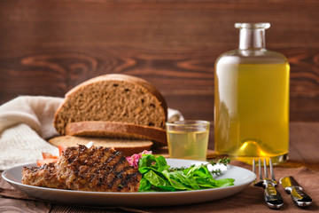 Grilled beef cutlet with fresh salad, brown bread and moonshine on rustic wooden table