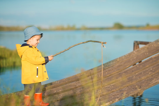Picturesque scene of cute little boy fishing from wooden dock on magical lake at sunny summer day, vivid colors