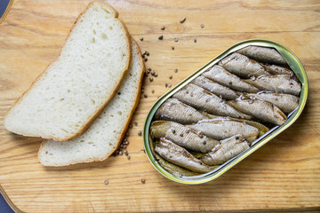 Open sprats can and sliced bread with spices on white background close up