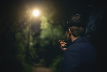 Detective agent is smoking a smoking pipe in night park.