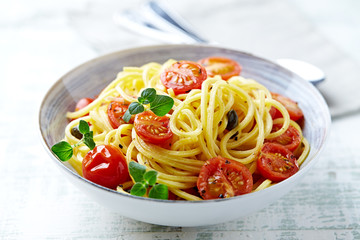 Spaghetti pasta with cherry tomatoes and fresh herbs in a small bowl. Bright wooden background. Close up.