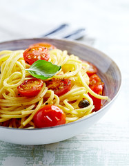 Spaghetti pasta with cherry tomatoes, capers and fresh herbs in a small bowl. Bright wooden background. Close up