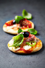 Mini pizzas with ham, mozzarella cheese, jalapeno pepper, black olives and fresh basil on dark...