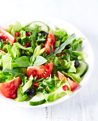 Salad with black Olives, red and yellow Tomatoes, Feta Cheese and Pommegranate Seeds on bright wooden Background. Healthy Snack Idea. Close up.