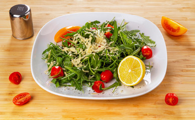 Arugula salad with cherry tomatoes and lemon on a white plate.