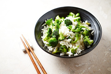 Cooked rice with fried broccoli on bright stone background.