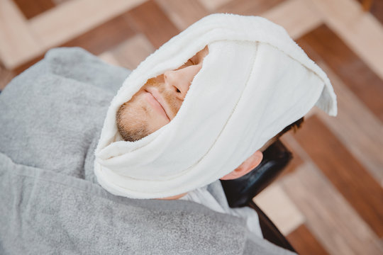 Barber steam face skin of man with hot towel before royal shave in Barbershop