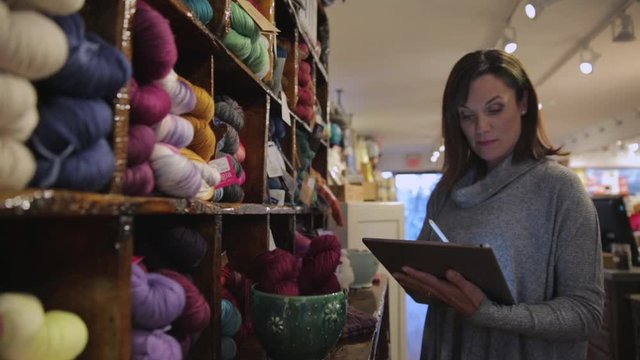 Yarn store owner taking inventory with digital tablet