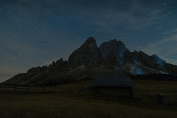 Night shot full of stars of trail in countryside with huts and puez odle sass de putia in background during autumn