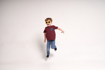 Little sweet boy in yellow glasses jumping on minimalistic white background