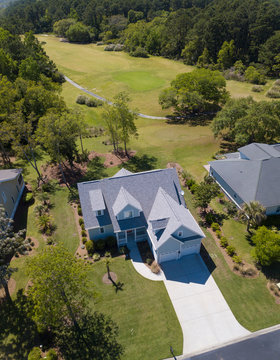 Aerial view of new home on beautiful wooded lot with golf course behind it.