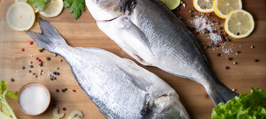 fresh fish with lemon, salt and pepper on wooden board