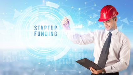 Handsome businessman with helmet drawing STARTUP FUNDING inscription, contruction business concept