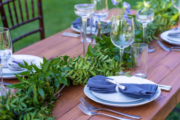 Beautifully decorated wooden table in a summer open-air cafe. Green branch and fresh flowers table decoration
