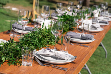 Beautifully decorated wooden table in a summer open-air cafe. Green branch and fresh flowers table decoration