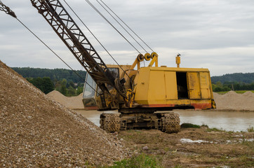 Excavator working in the river gravel quarry against the background of the forest. Extraction of natural resources.