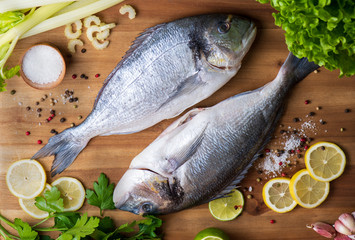 fresh fish with lemon, salt and pepper on wooden board