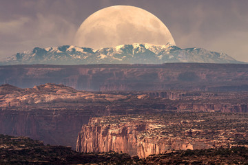 Full moon at it's perigee rising behind La Sal Mountains in Canyonlands National Park during sunset - obrazy, fototapety, plakaty