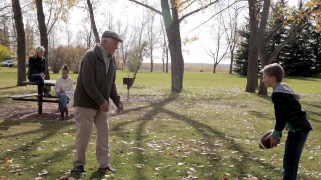 Grandfather And Grandson Throwing Football In Sunny Autumn Park