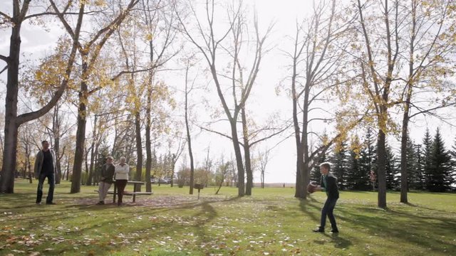 Father And Son Throwing Football In Sunny Autumn Park With Grandparents Watching