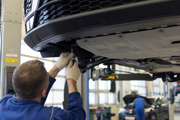 The car is lifted on a lift in a car service for repair. A professional mechanic is repairing a car.