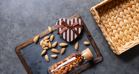 Heart shaped gift box with wild almonds around and empty wicker basket. Top view.