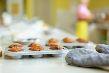 Confectioner took out freshly baked muffins in a baking dish on the table from the oven