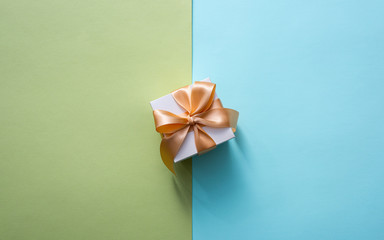 Obraz na płótnie Canvas Gift box with golden tied bow, on two-color background. Top view holiday background.