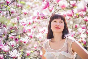 beautiful dark-haired woman among branches of magnolia. first flowers in trees in spring.