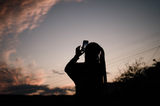 silhouette of girl who take photo of sunset