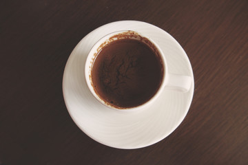 little white cup with hot black coffee on a brown table