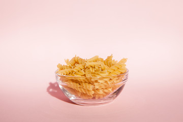 Beautiful italian rotini pasta in glass bowl on pink background