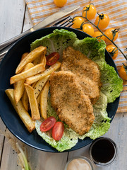 food, breaded chicken fillet with cherry tomatoes, french fries, lettuce, herbs, sandwich, on a black background, serving example