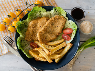 food, breaded chicken fillet with cherry tomatoes, french fries, lettuce, herbs, sandwich, on a black background, serving example