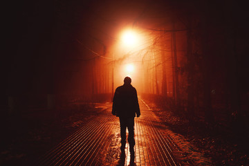 Sad man alone walking along the alley in night foggy park. Back view