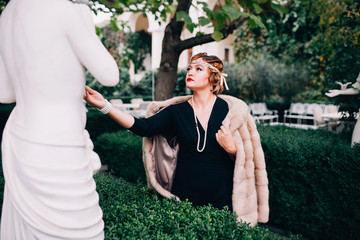 a gorgeous woman in a fur cape and a diadem on her head walks through her garden surrounded by...