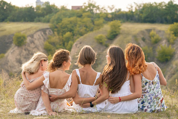 Shoot from back. The company of female friends having fun, hugs each other and enjoy hills landscape