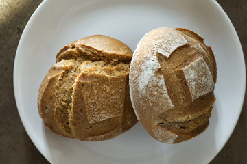 Two soft fresh baked white bread with a crispy crust on a white plate on textured table