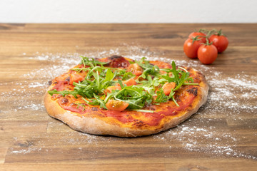 homemade pizza margherita with tomato sauce, mozzarella, served on a floured wooden table decorated with fresh tomatoes
