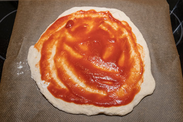 homemade pizza dough with tomato sauce on baking paper