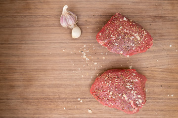 two raw peppered beef steak on dark wooden cutting board with garlic and sea salt