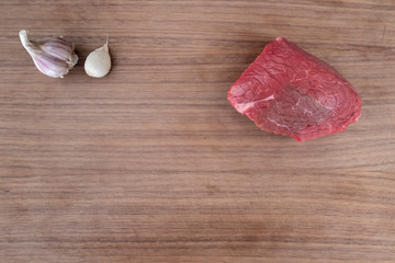 raw beef steak on dark wooden cutting board with garlic