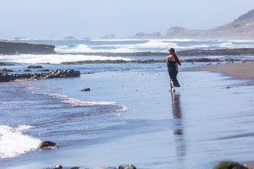 Young girl with a black dress and hut walking at the wet coast in a beach inside an awe natural scenery at Chilean coast. Enjoying vacations with a relaxing walk inside a tranquil beach scene
