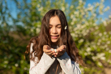 Portrait of a young beautiful teenager girl in a blooming spring green garden blows petals off with her palms